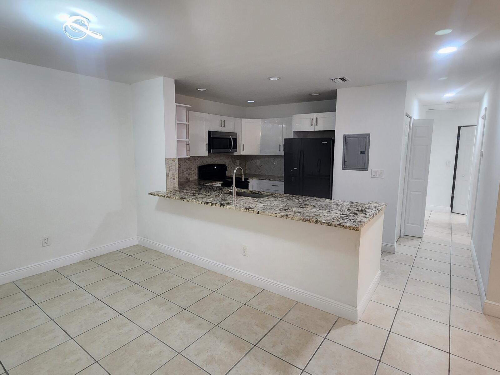 A kitchen with white cabinets, granite countertops, and black appliances overlooks a tiled dining area — 6013 10th Avenue N # 208, FL 33463, FL