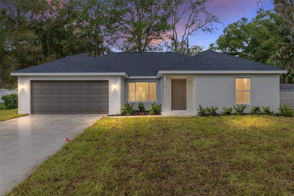 A single-story house with a gray garage, white stucco exterior, and a dark shingled roof — 20 MALAUKA COURSE, OCKLAWAHA, FL