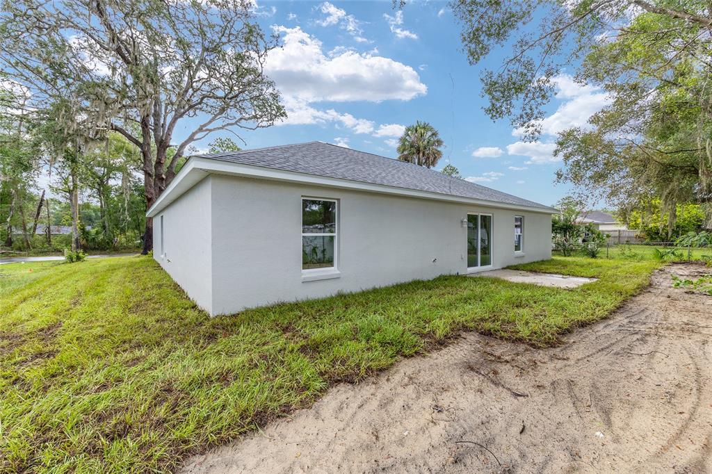 The exterior rear view of a single-story house with a gray roof and stucco walls — 20 MALAUKA COURSE, OCKLAWAHA, FL
