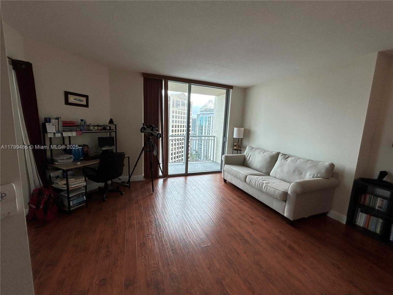 A living room features wood-look flooring, a beige sofa, a desk, and a balcony view — 9066 SW 73rd Ct # 1504, Miami FL 33156, MIAMI, FL