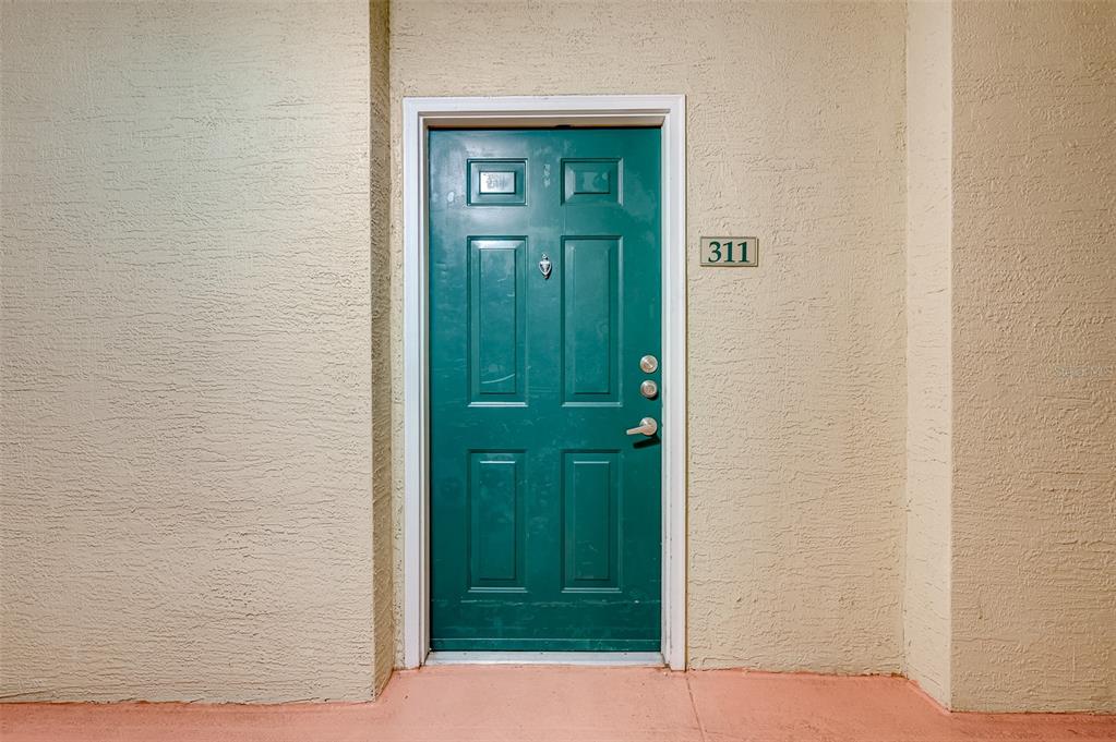 A teal front door with the number 311 is set into a textured beige wall — 1216 S MISSOURI AVENUE UNIT 311, CLEARWATER, FL