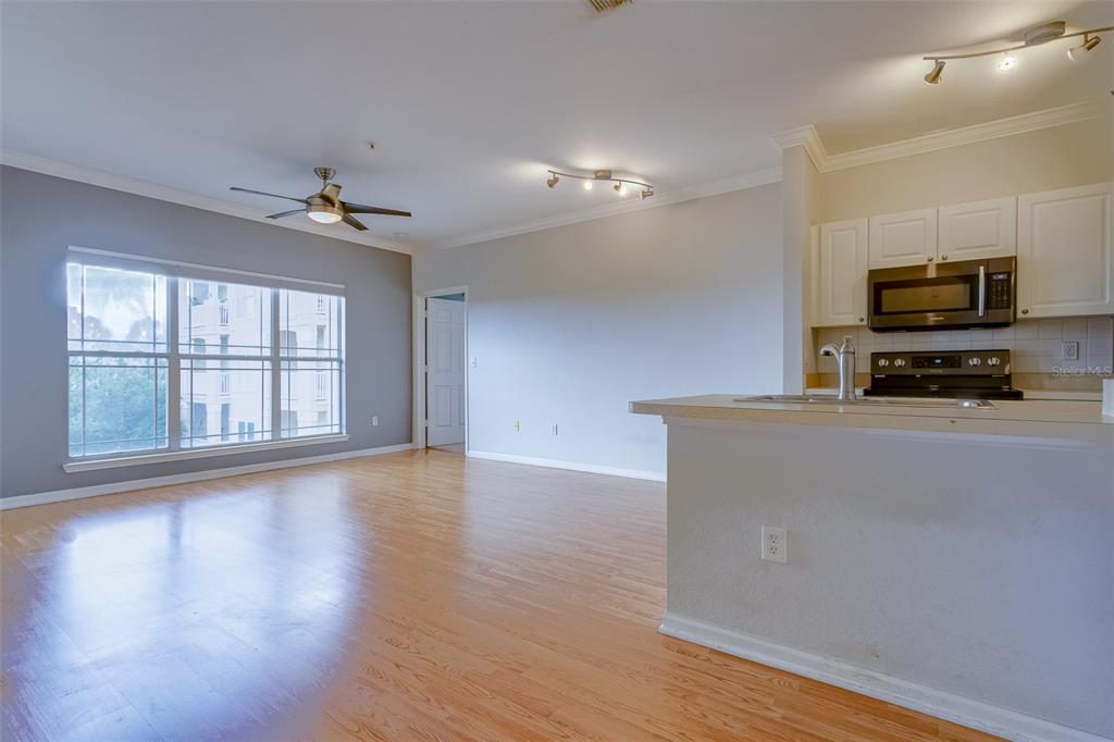 A living room with wood flooring and a ceiling fan opens to a kitchen area — 1216 S MISSOURI AVENUE UNIT 311, CLEARWATER, FL