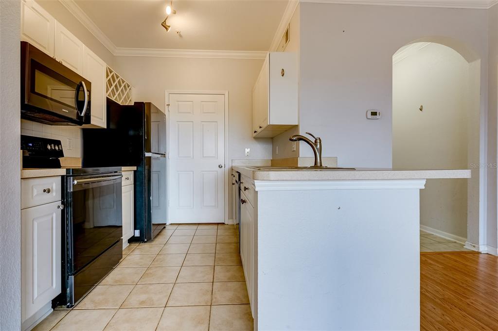 A kitchen features white cabinets, black appliances, tile flooring, and a peninsula with a sink — 1216 S MISSOURI AVENUE UNIT 311, CLEARWATER, FL