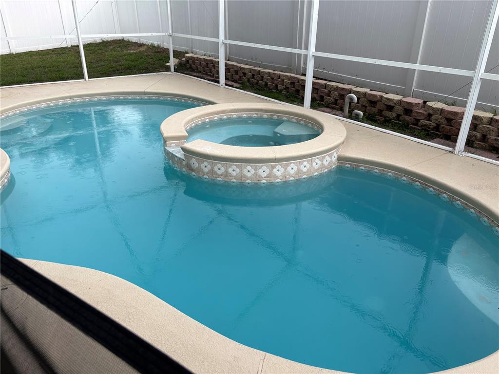 A swimming pool with an integrated spa is enclosed by a screen and white fencing — 2830 PANKAW LANE, VALRICO, FL