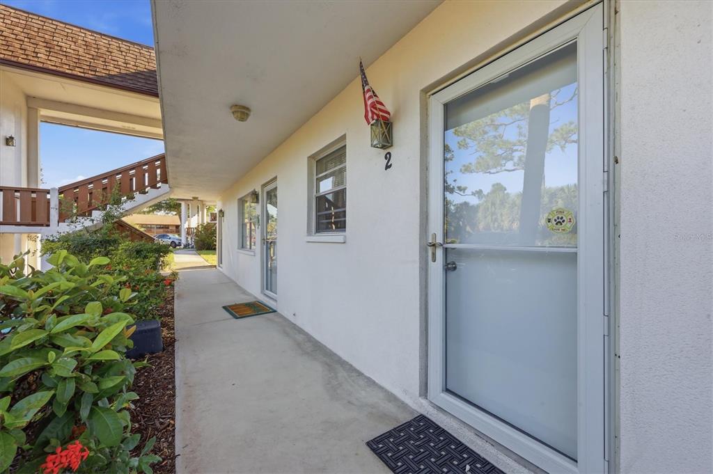 A concrete walkway leads past the exterior doors of a multi-unit residential building — 2 QUAILS RUN BOULEVARD UNIT 2104, ENGLEWOOD, FL