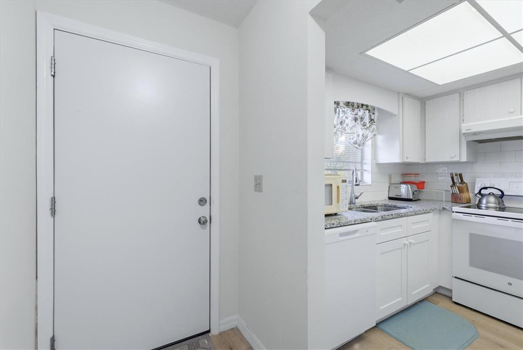 A white door stands next to a kitchen featuring white cabinets and granite countertops — 2 QUAILS RUN BOULEVARD UNIT 2104, ENGLEWOOD, FL