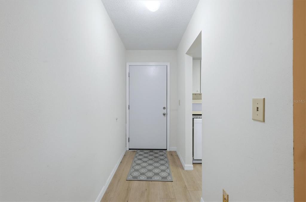 A narrow entryway features light wood-look flooring, white walls, and a white front door — 2 QUAILS RUN BOULEVARD UNIT 2104, ENGLEWOOD, FL