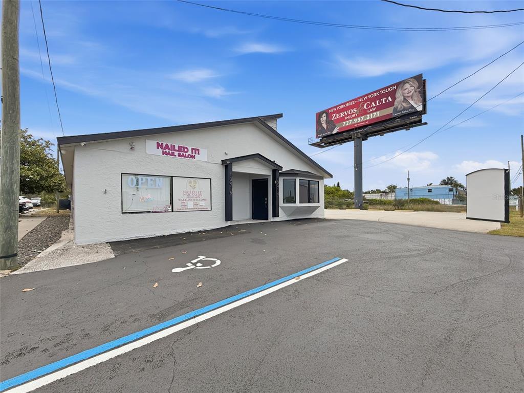 A white, single-story commercial building with a nail salon sign and an adjacent billboard — 13414 US HIGHWAY 19, HUDSON, FL