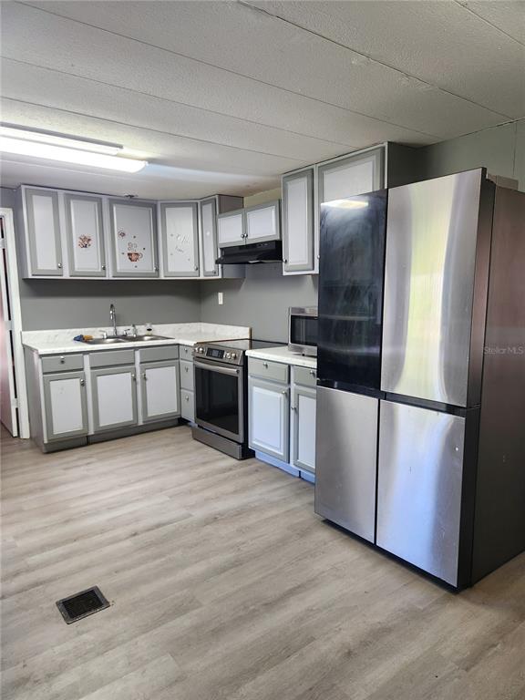 A kitchen features gray and white cabinets, stainless steel appliances, and light wood-look flooring — 900 NW 42ND PLACE, OCALA, FL