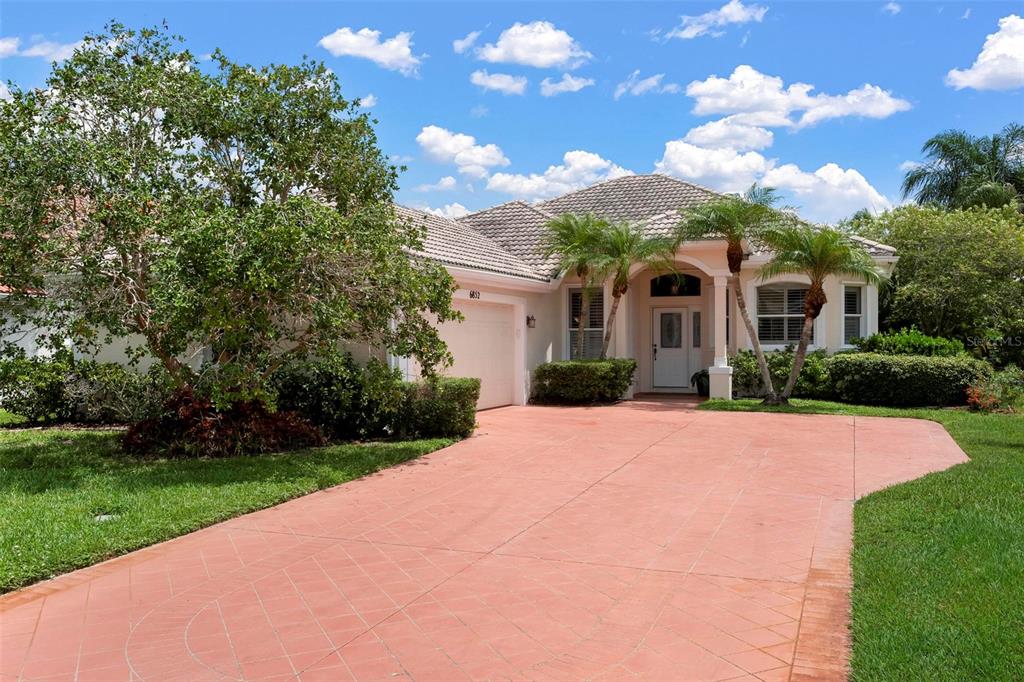 A single-story house with a tiled roof, a red paved driveway, and palm trees — 6852 SAGEBRUSH CIRCLE, SARASOTA, FL