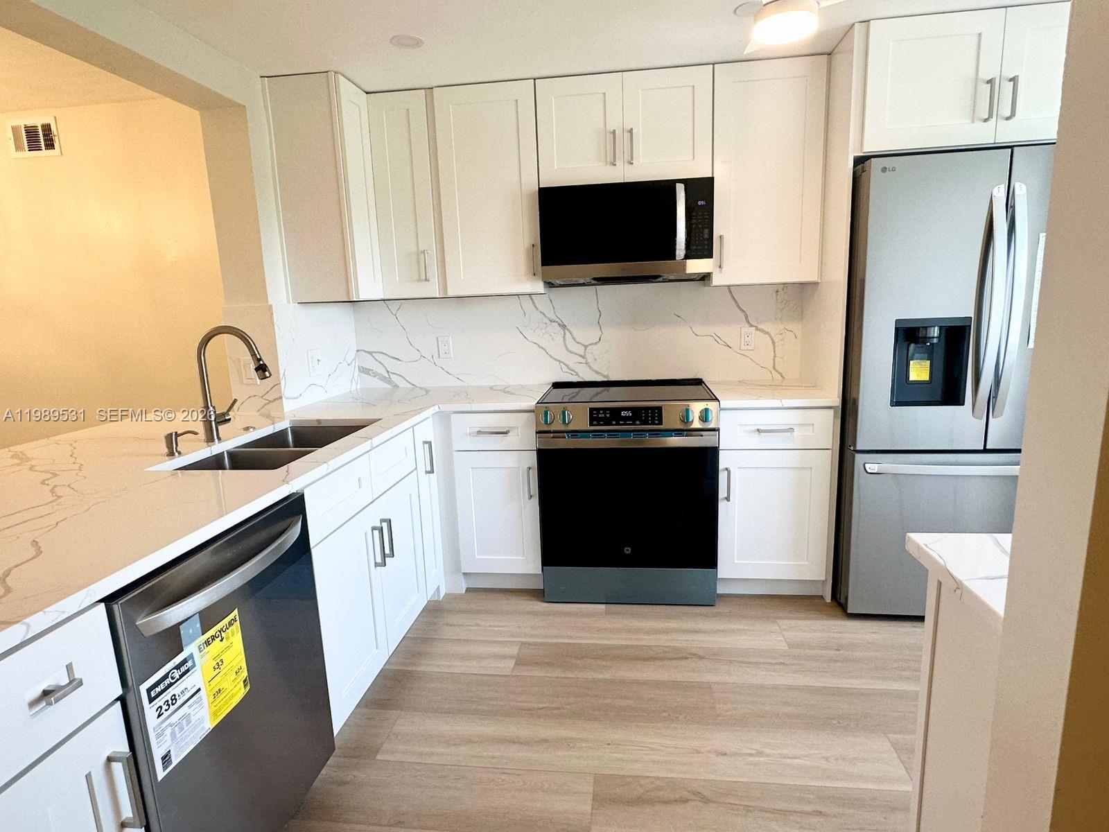 A kitchen features white cabinets, marble-patterned countertops, stainless steel appliances, and light wood flooring — 4098 Yarmouth  E # 4098, Boca Raton FL 33434, BOCA RATON, FL