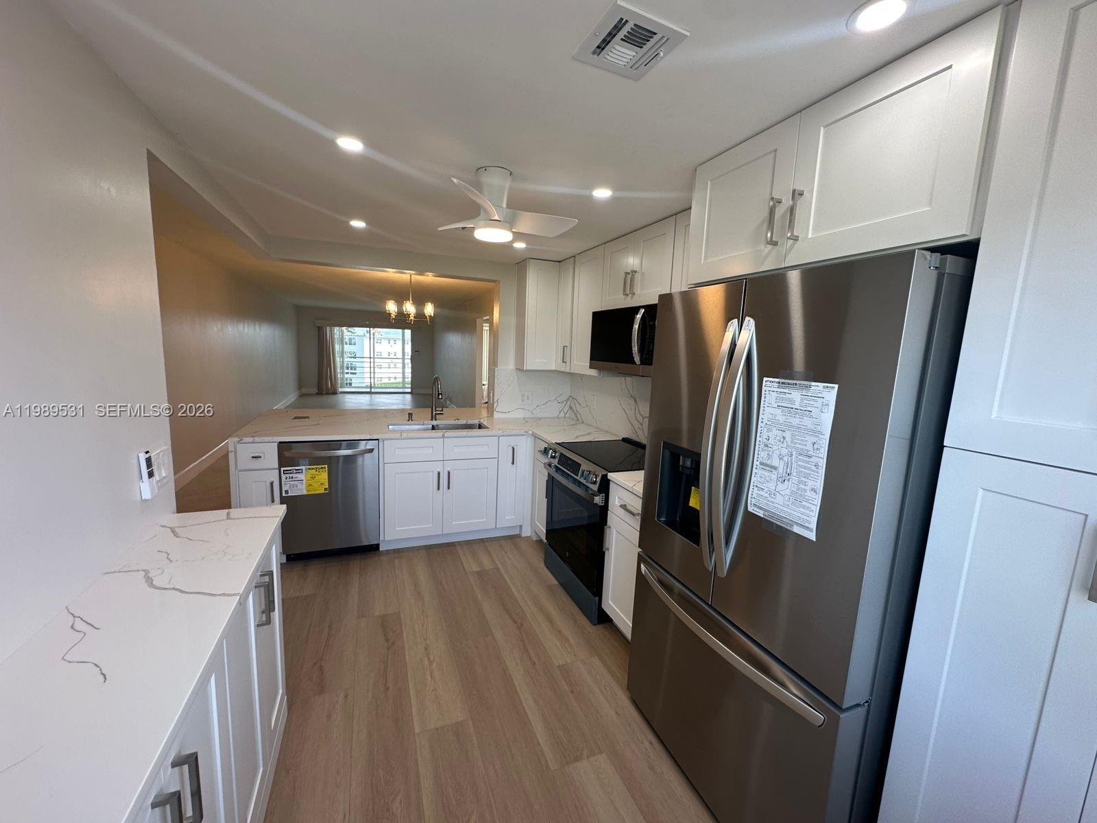 A modern kitchen features white cabinets, stainless steel appliances, and light wood-look flooring — 4098 Yarmouth  E # 4098, Boca Raton FL 33434, BOCA RATON, FL
