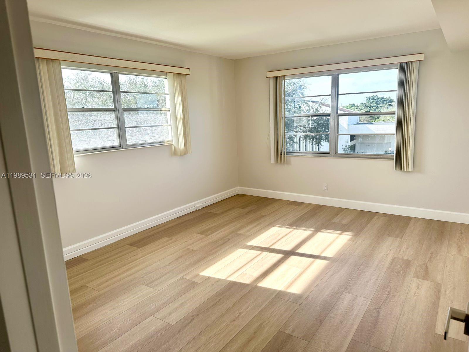 An empty room features light wood-look flooring, neutral walls, and two windows with vertical blinds — 4098 Yarmouth  E # 4098, Boca Raton FL 33434, BOCA RATON, FL