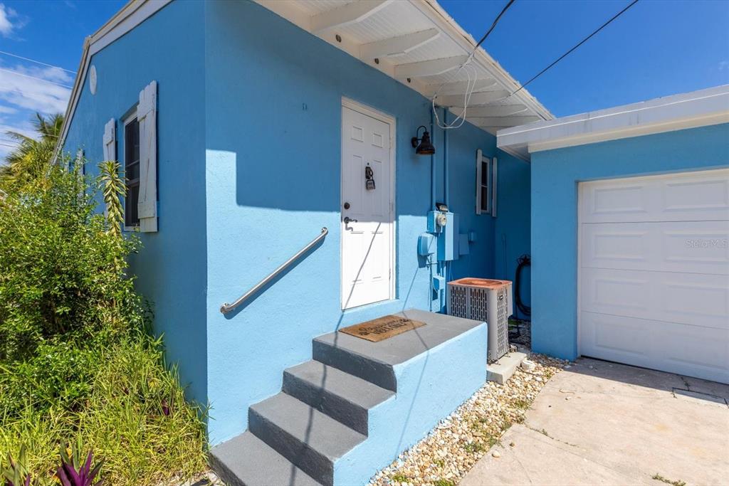A bright blue exterior wall features a white door, concrete steps, and a garage door — 301 GRANADA STREET, FORT PIERCE, FL