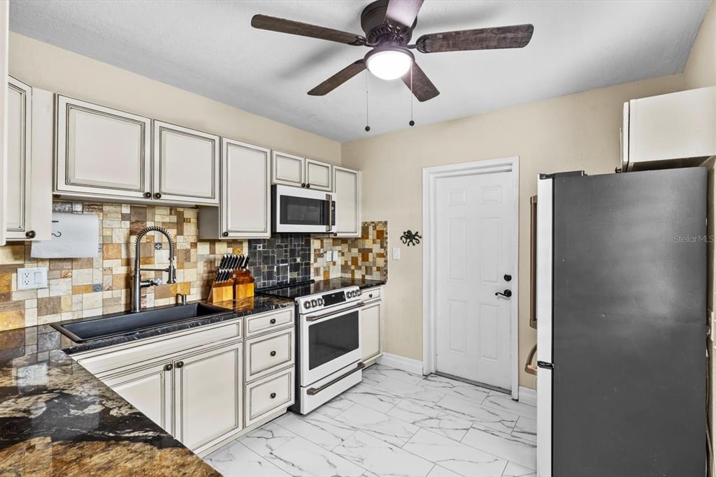 A kitchen features white cabinets, a black sink, a tiled backsplash, and a ceiling fan — 301 GRANADA STREET, FORT PIERCE, FL