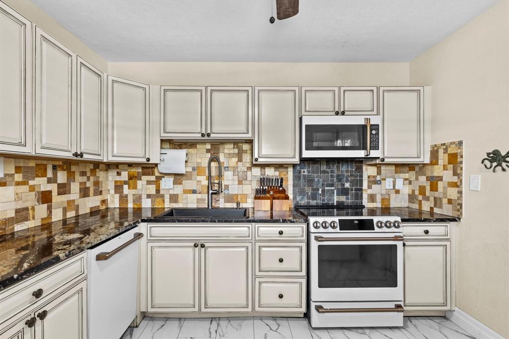 A kitchen features off-white cabinets, dark granite countertops, a mosaic tile backsplash, and white appliances — 301 GRANADA STREET, FORT PIERCE, FL