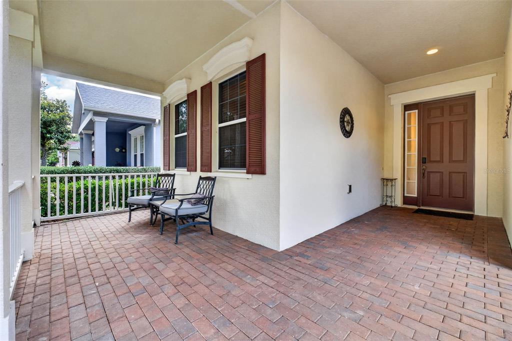 A covered brick porch features two chairs, red shutters, and a brown front door — 111 FLAME VINE WAY, GROVELAND, FL
