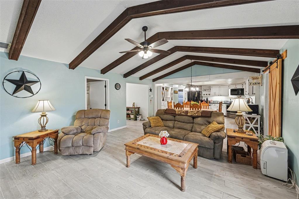 A living room features vaulted ceilings with exposed wooden beams, light-colored flooring, and farmhouse decor — 429 MANOR BOULEVARD, PALM HARBOR, FL