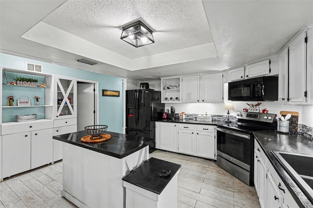 A kitchen features white cabinetry, black countertops, a central island, and light-colored wood-look flooring — 429 MANOR BOULEVARD, PALM HARBOR, FL