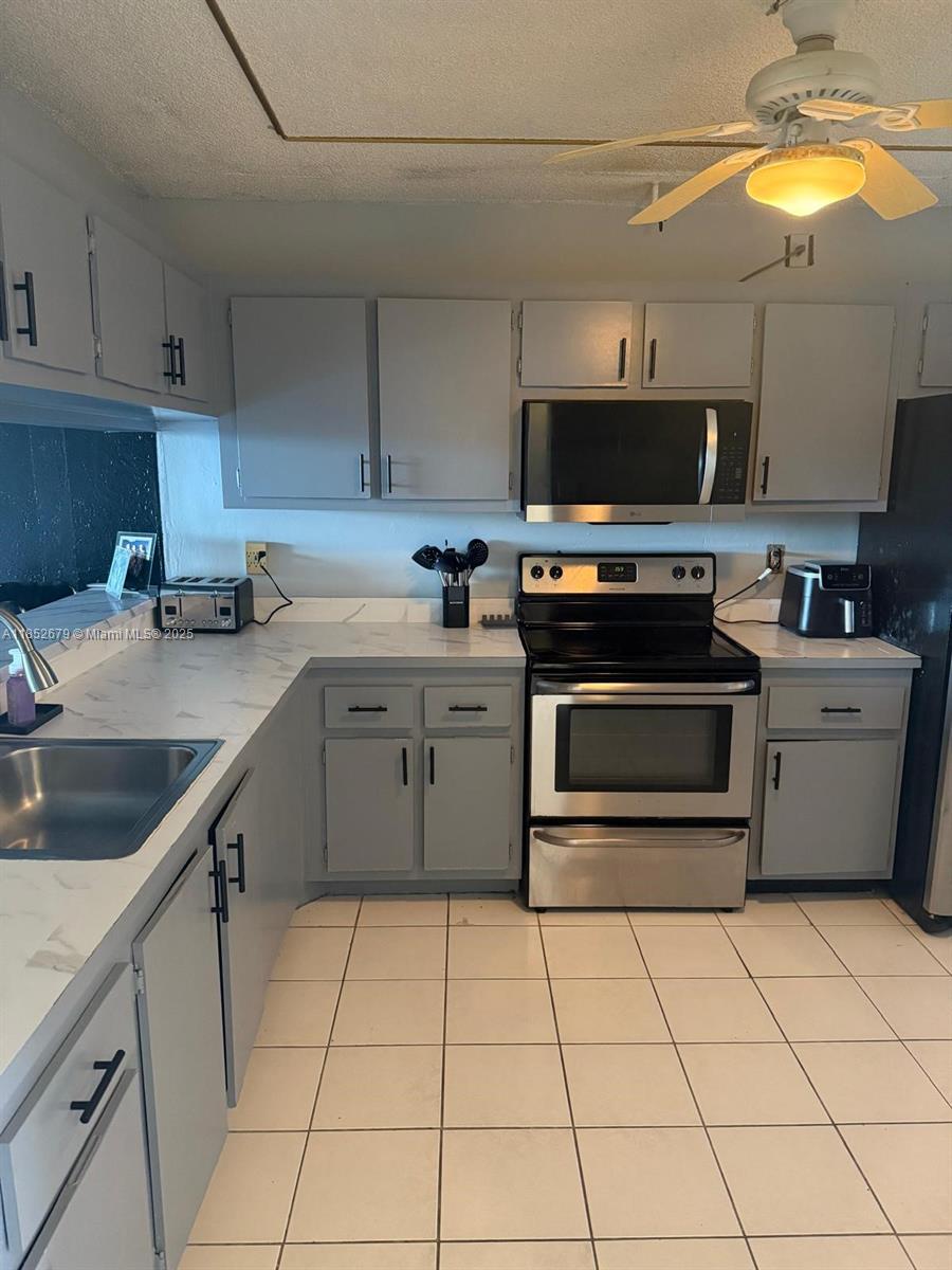 A kitchen features grey cabinets, stainless steel appliances, white countertops, and white tile flooring — 8040 Hampton Blvd # 512, North Lauderdale FL 33068, NORTH LAUDERDALE, FL