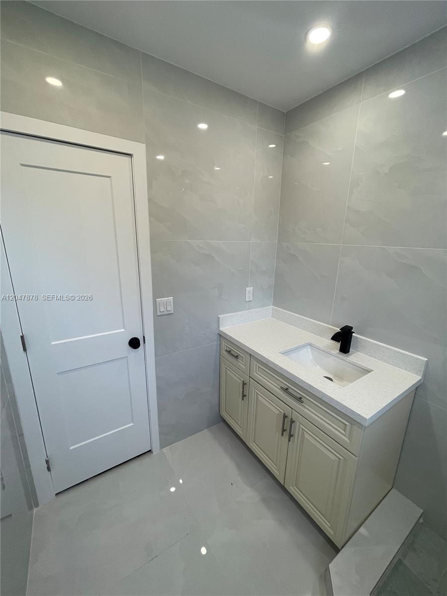 A bathroom features a white vanity with a black faucet against light gray tiled walls — 2352 SW 26th Ln, Miami FL 33133, MIAMI, FL