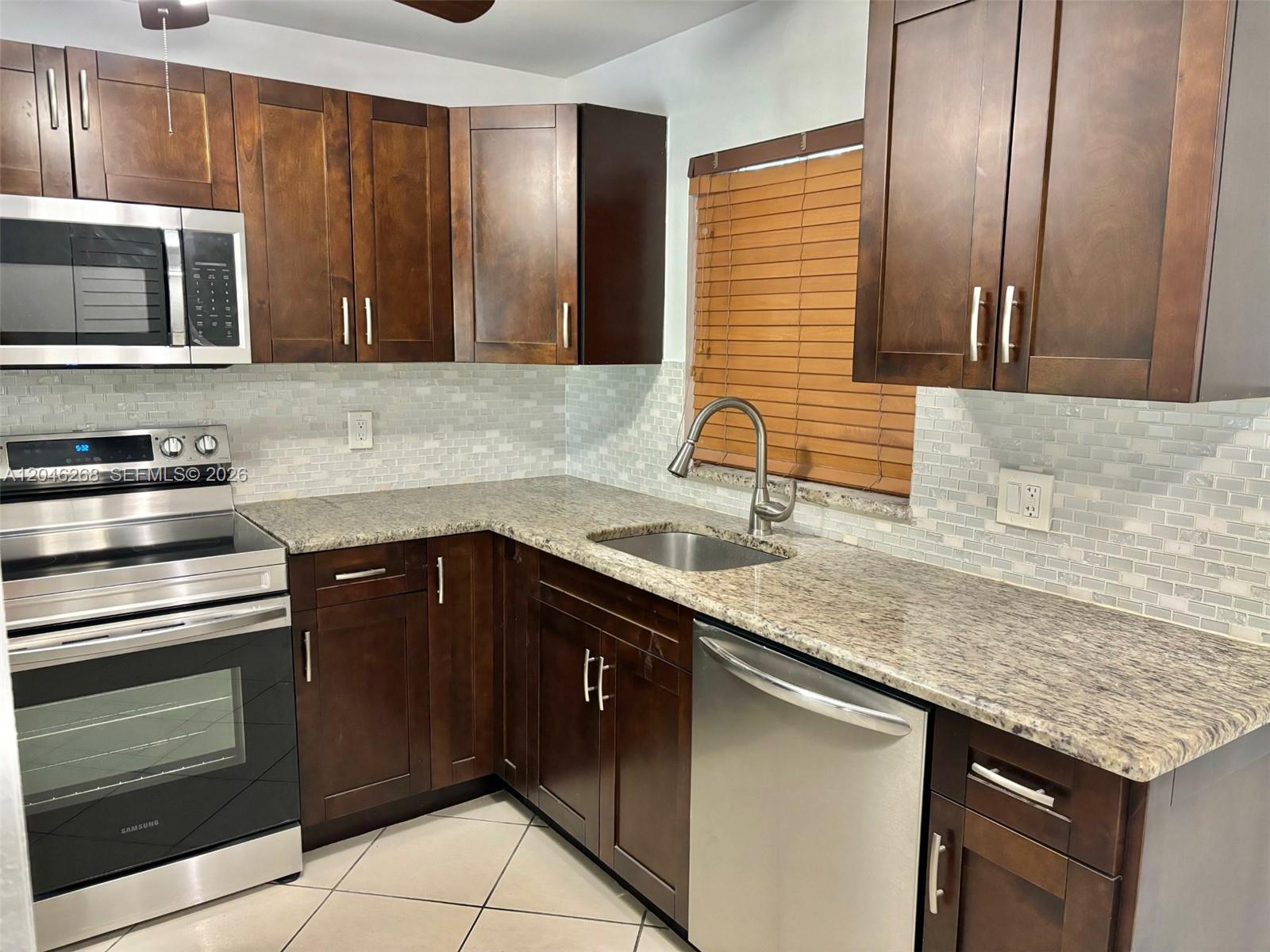 A kitchen features dark wood cabinets, granite countertops, stainless steel appliances, and a tiled backsplash — 9411 Evergreen Pl # 303, Davie FL 33324, DAVIE, FL
