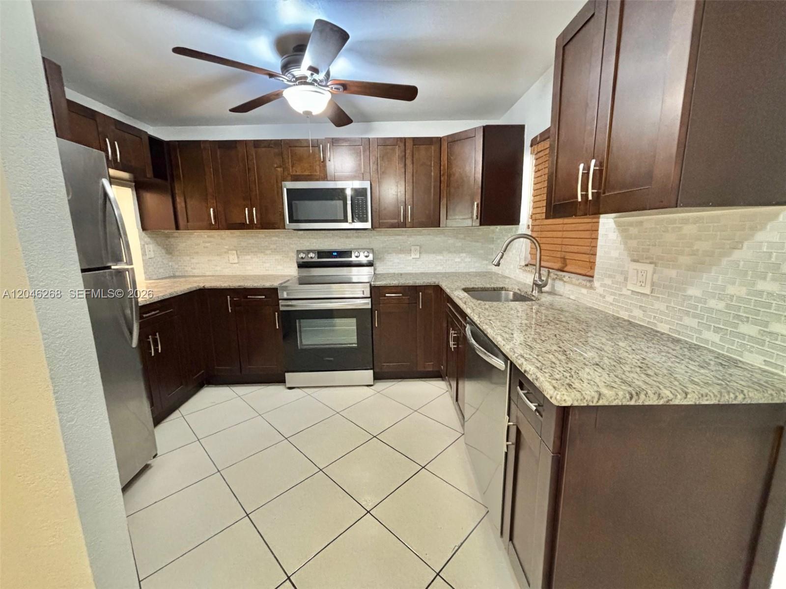 A kitchen features dark wood cabinets, granite countertops, stainless steel appliances, and tiled flooring — 9411 Evergreen Pl # 303, Davie FL 33324, DAVIE, FL