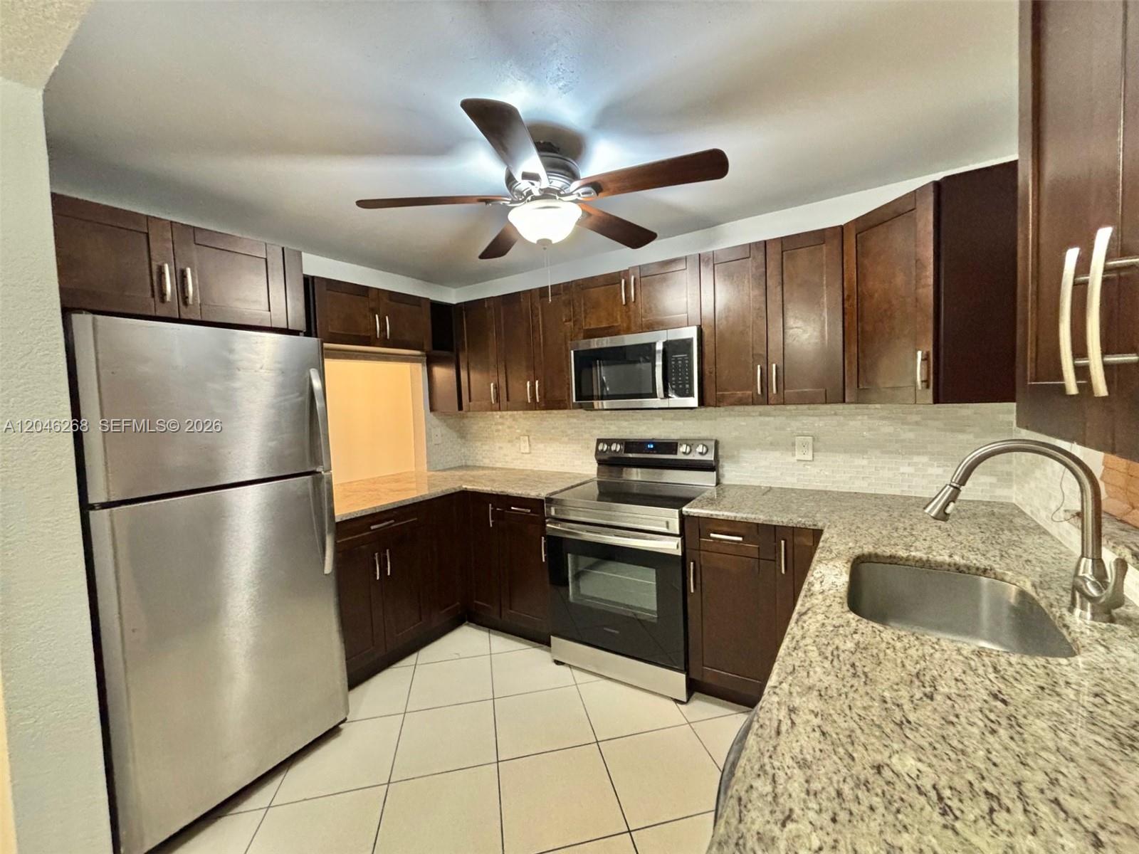 A kitchen features dark wood cabinets, stainless steel appliances, granite countertops, and light tile flooring — 9411 Evergreen Pl # 303, Davie FL 33324, DAVIE, FL