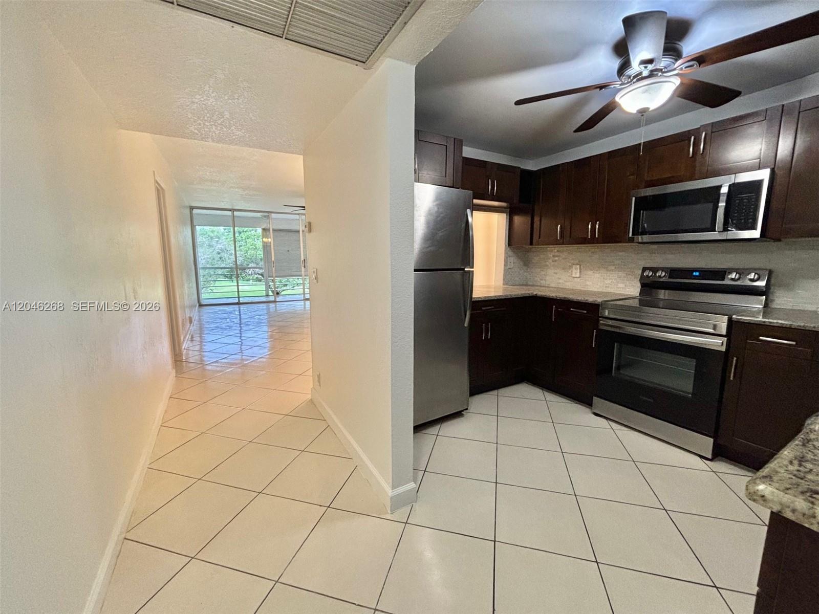A kitchen with dark wood cabinets and stainless steel appliances opens to a tiled hallway — 9411 Evergreen Pl # 303, Davie FL 33324, DAVIE, FL