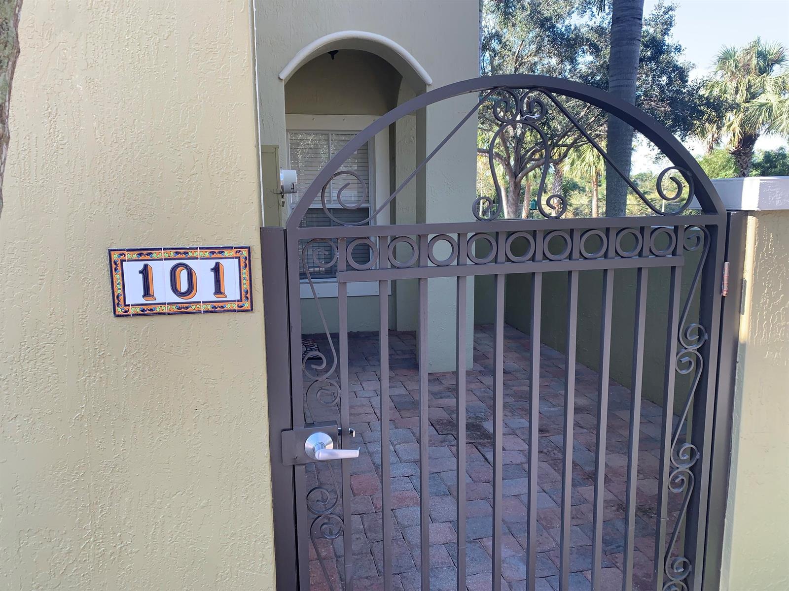 A metal gate with decorative scrollwork stands before a paved entryway marked with number 101 — 101 Lake Monterey Circle, Boynton Beach FL 33426, BOYNTON BEACH, FL