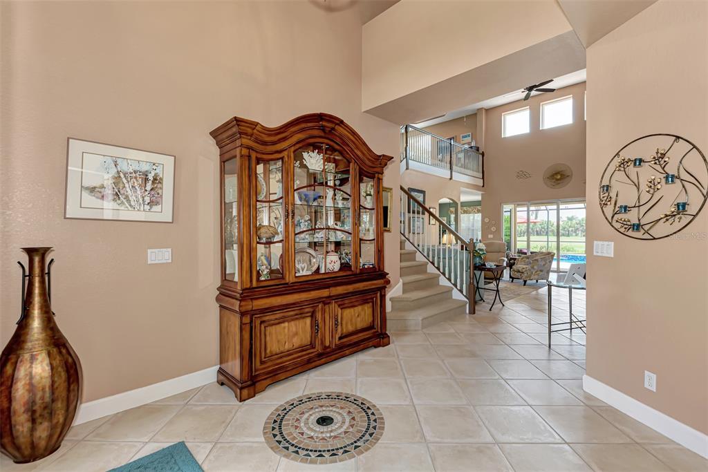 A tiled entryway features a large wooden china cabinet, a decorative floor medallion, and stairs — 13392 GOLF POINTE DRIVE, PORT CHARLOTTE, FL