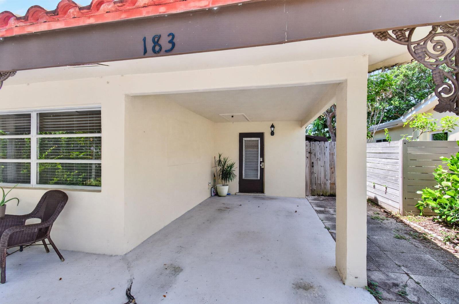 A covered concrete carport leads to a dark brown front door with a glass insert — 183 Harvard Drive, Lake Worth FL 33460, LAKE WORTH, FL