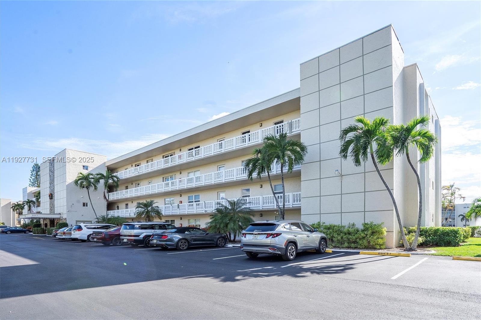 A multi-story apartment building features white balconies and a parking lot with several cars — 324 SE 10th St # 203, Dania Beach FL 33004, DANIA BEACH, FL