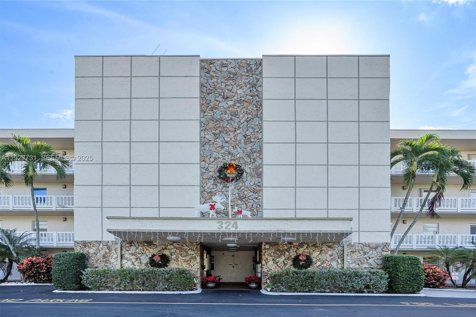The exterior of a multi-story building features a stone-accented entrance with holiday decorations — 324 SE 10th St # 203, Dania Beach FL 33004, DANIA BEACH, FL