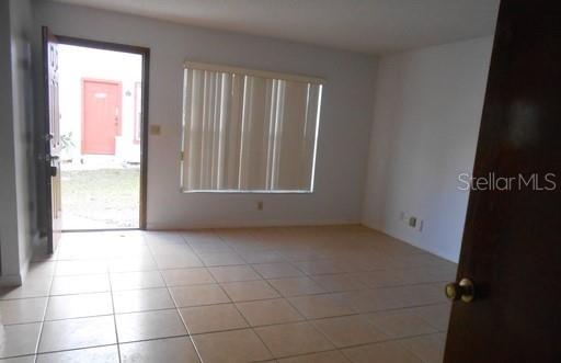 A living room with light-colored tile flooring, a window with vertical blinds, and an open door — 2007 KELLEY AVENUE, KISSIMMEE, FL