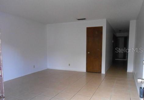 An empty room with white walls, beige tile flooring, and a wooden door — 2007 KELLEY AVENUE, KISSIMMEE, FL