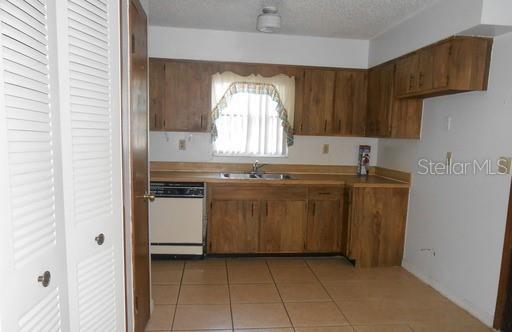 A kitchen features wood cabinets, tile flooring, a dishwasher, and a window above the sink — 2007 KELLEY AVENUE, KISSIMMEE, FL