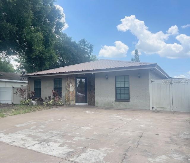 The exterior of a single-story house features a metal roof, stone accents, and a concrete driveway — 3804 W HAMILTON AVENUE, TAMPA, FL