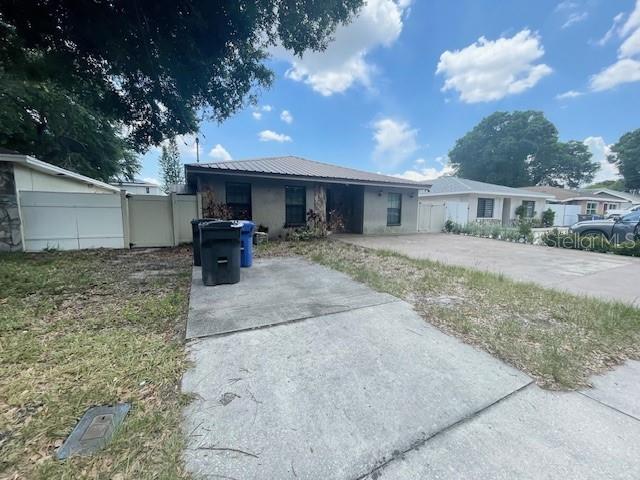 A single-story house with a metal roof and a concrete driveway sits under a sky — 3804 W HAMILTON AVENUE, TAMPA, FL
