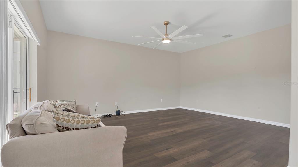 A living room features dark wood-look flooring, beige walls, and a modern ceiling fan — 545 FAIRHAVEN DRIVE, DAVENPORT, FL