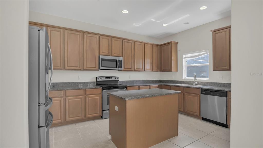 A kitchen features light wood cabinets, granite countertops, stainless steel appliances, and a central island — 545 FAIRHAVEN DRIVE, DAVENPORT, FL