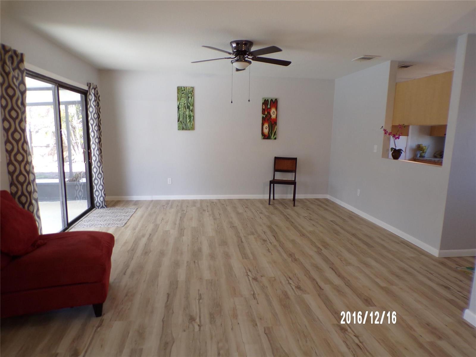 A spacious living room features light wood-look flooring, a ceiling fan, and a sliding glass door — 2265 14th Avenue SW, Vero Beach FL 32962, VERO BEACH, FL