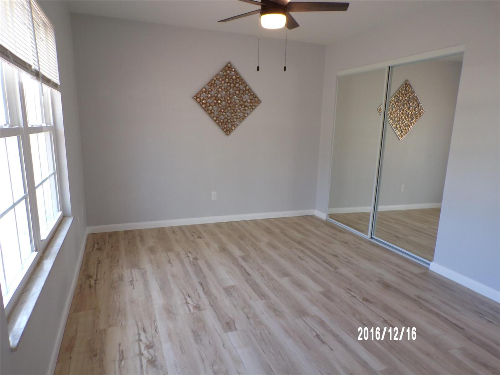 An empty bedroom features light wood-look flooring, gray walls, a ceiling fan, and mirrored closets — 2265 14th Avenue SW, Vero Beach FL 32962, VERO BEACH, FL