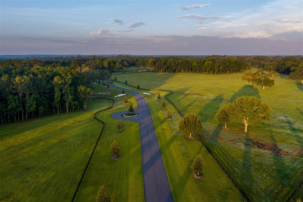 An aerial view shows a paved driveway winding through a large, grassy, fenced pasture — 11771 NW 50TH LANE ROAD, OCALA, FL