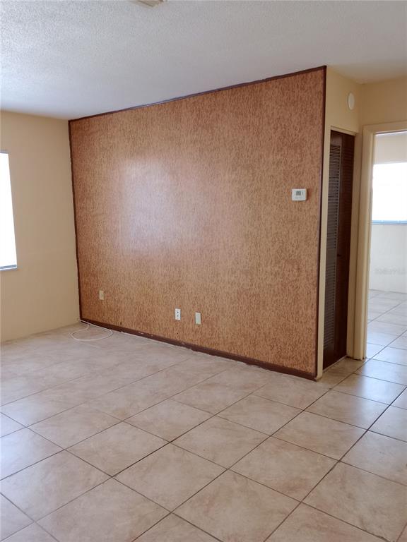 An empty room features tan tile flooring and a large wall with textured brown paneling — 1217 KENNEDY ROAD UNIT 58, DAYTONA BEACH, FL
