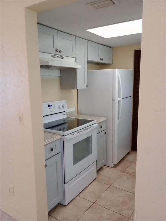 A small kitchen features light gray cabinets, white appliances, and beige tile flooring — 1217 KENNEDY ROAD UNIT 58, DAYTONA BEACH, FL