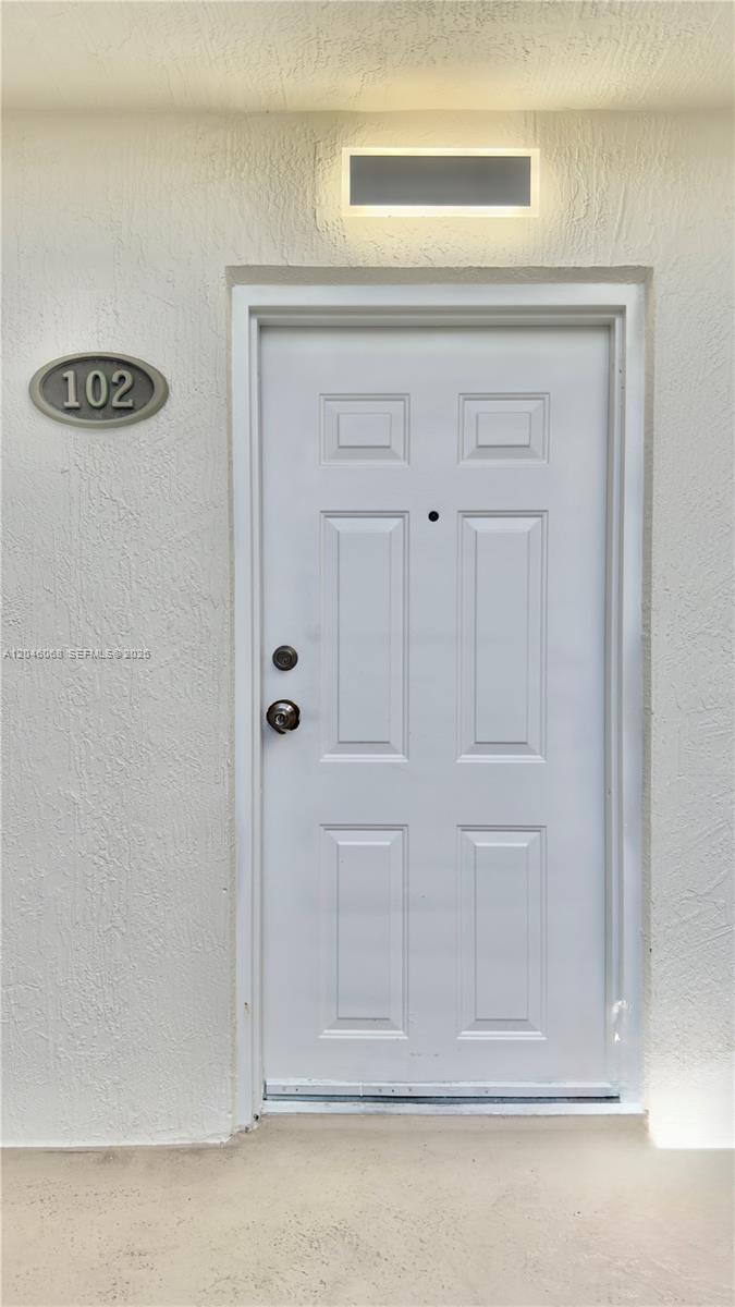 A white six-panel door with a number 102 plaque and an exterior light fixture — 630 85th St # 102, Miami Beach FL 33141, MIAMI BEACH, FL