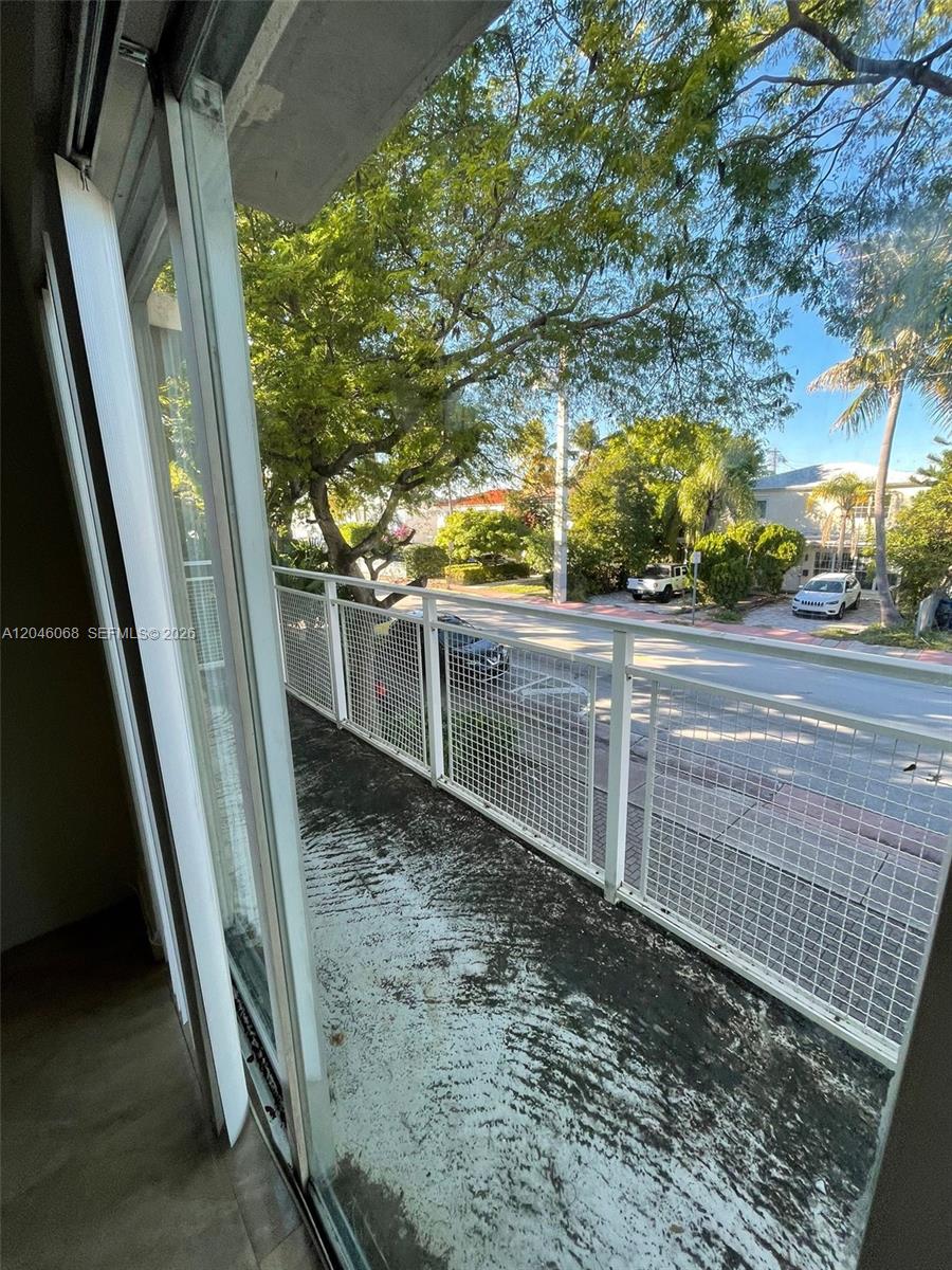 A balcony with a white metal railing overlooks a street lined with trees and houses — 630 85th St # 102, Miami Beach FL 33141, MIAMI BEACH, FL
