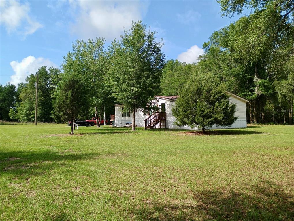 A white manufactured home sits on a large grassy lot surrounded by mature trees — 9889 NW 9TH COURT, BRANFORD, FL