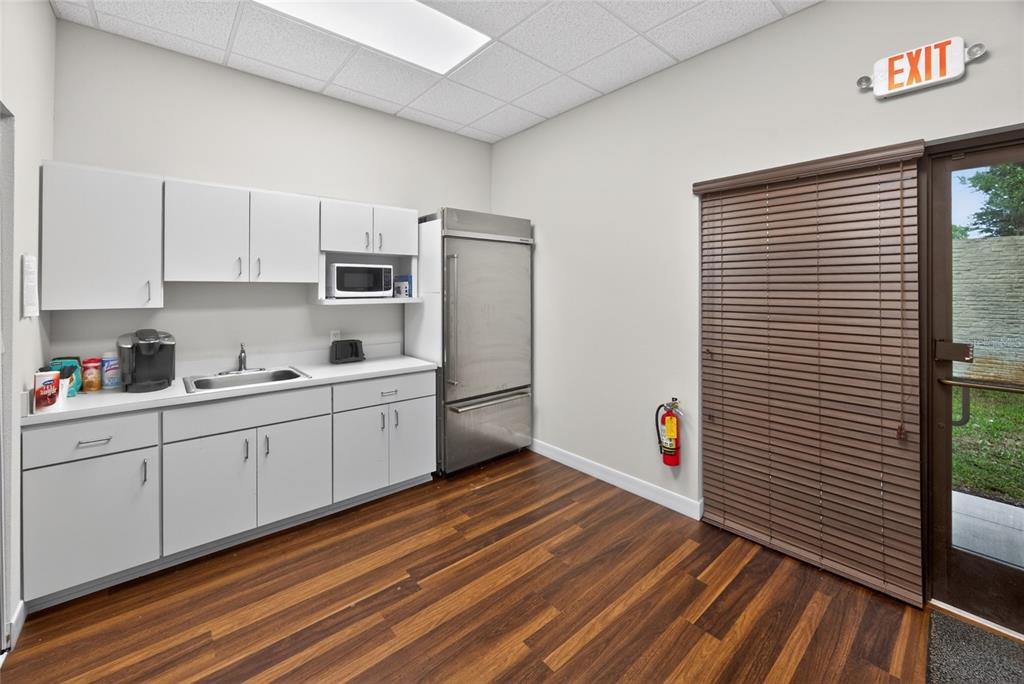 A breakroom features white cabinetry, a stainless steel refrigerator, a sink, and wood-look flooring — 4064 E STATE ROAD 44, WILDWOOD, FL